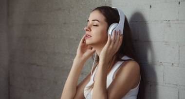 Genç kadın duvarının yakınında kulaklık ile müzik dinlemek