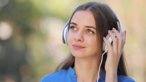 Mujer linda escuchando música al aire libre con auriculares, cámara lenta — Vídeo de stock