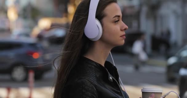 Mujer moderna con taza de café en la ciudad escuchando música en auriculares, estilo de vida — Vídeo de stock