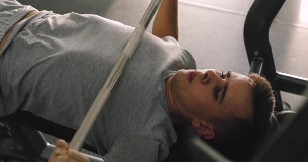 Jovem iniciante homem se exercitando com barbell no ginásio fazendo supino — Vídeo de Stock