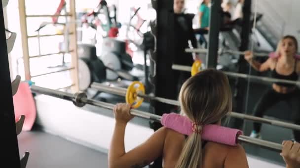 Jovem instrutor de fitness treinando mulher fazer agachamentos exercício com barra — Vídeo de Stock