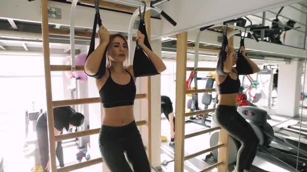 Young woman make exercise for low abs muscle hunging on horizontal bar in fitness center — Stock Video