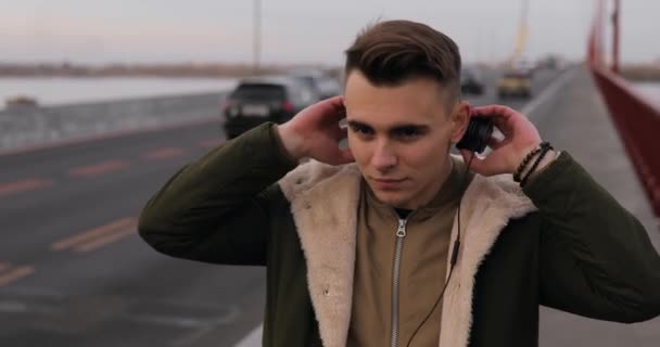 Junger Mann Hört Musik Mit Kopfhörern Auf Der Stadtbrücke — Stockvideo