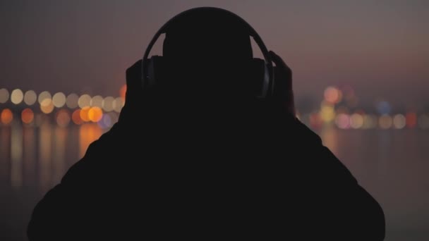 人听音乐的剪影在晚上城市与耳机 后视镜 — 图库视频影像