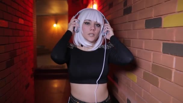 性感的不寻常的女孩听音乐与耳机穿过红灯走廊 — 图库视频影像