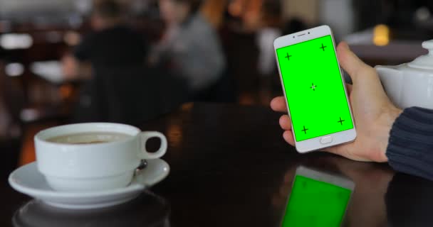 Зеленый экран смартфона, рука держит цифровой дисплей в кафе — стоковое видео