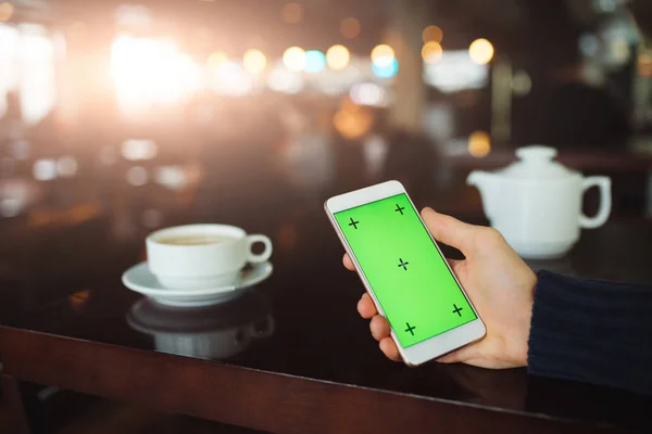 智能手机的绿色屏幕 手拿数字显示在咖啡馆背景 — 图库照片