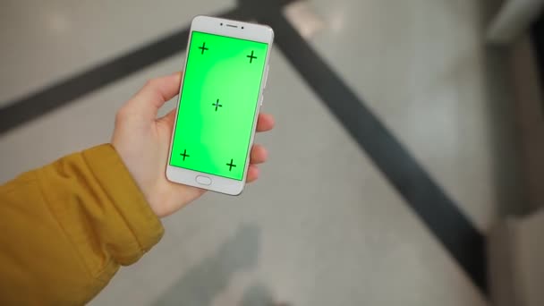 Мужчина держит в руках смартфон с зеленым экраном, проходящим через торговый центр — стоковое видео