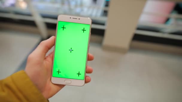 Αρσενική χέρι που κρατά το smartphone με πράσινη οθόνη που διέρχεται από το εμπορικό κέντρο — Αρχείο Βίντεο