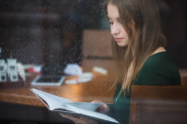 Livre de lecture femme dans le café, vue par la fenêtre mouillée le jour de pluie — Photo