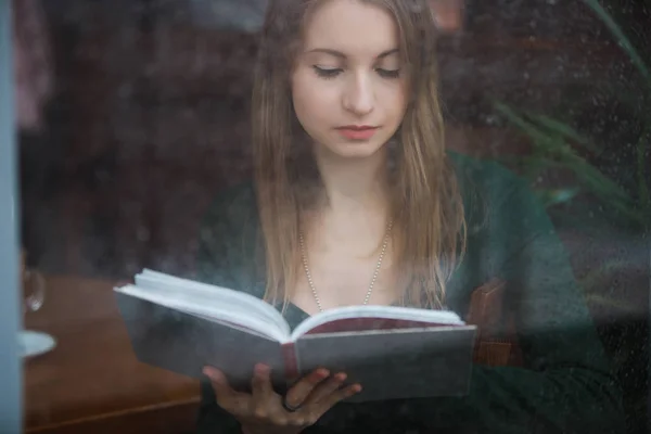 Livre de lecture femme dans le café, vue par la fenêtre mouillée le jour de pluie — Photo