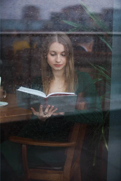 Livre de lecture femme dans le café, vue par la fenêtre mouillée le jour de pluie — Photo
