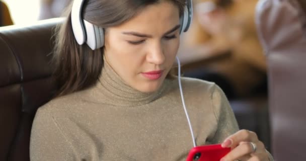 Retrato de mujer joven usando smartphone compartiendo las redes sociales en la cafetería con auriculares — Vídeos de Stock