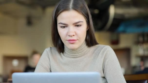 Молодая женщина-блоггер работает за ноутбуком в кафе, редактируя новое видео для своего блога — стоковое видео