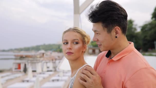 Casal jovem olhando para o mar, o homem mostra-lhe algo interessante — Vídeo de Stock