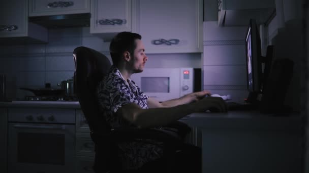 Man aan het werk met zijn video-editing in donkere keuken kamer, blauw licht scherm — Stockvideo