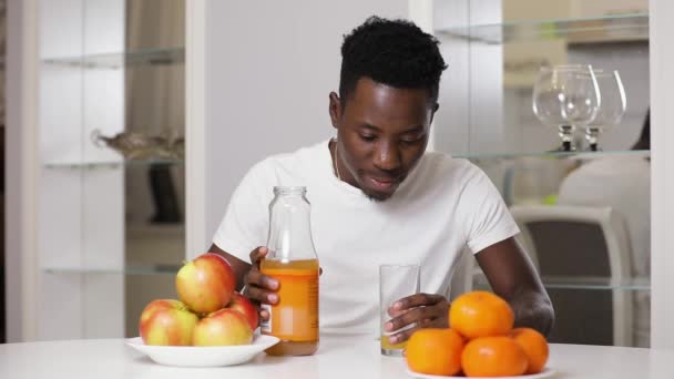 Hombre afroamericano bebiendo jugo en la cocina — Vídeos de Stock