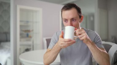 Genç komik adam, ev mutfak, çay içme açmak yüz ve kameraya gülümseyen