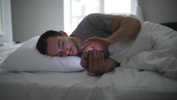 Man ligt in zijn bed met mobiele telefoon — Stockvideo