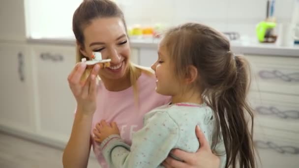 Счастливая мать дразнит дочь печеньем, играющим на кухне — стоковое видео