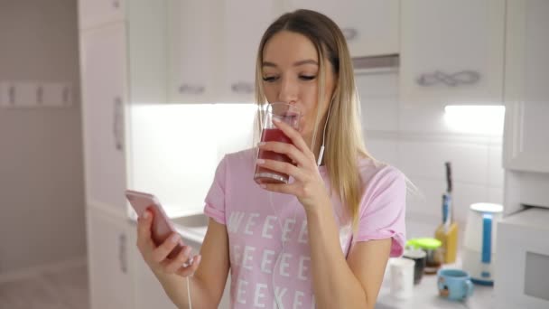 Gelukkig ochtend, vrouw drinken sap staande op de keuken thuis muziek beluisteren — Stockvideo