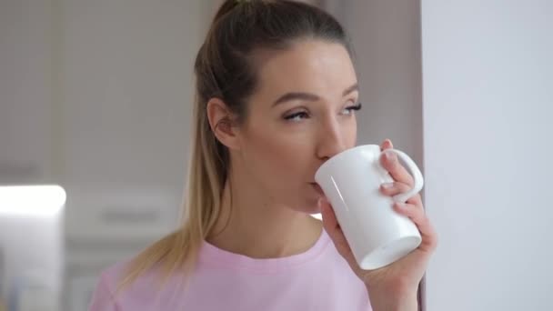 Młoda kobieta w różowy t thirt cieszyć się picie herbaty z cookie zimy w domu — Wideo stockowe