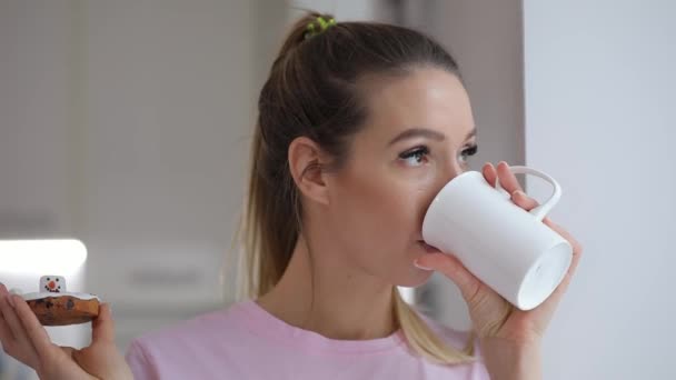 Mladá žena v růžové t khošile si, pít čaj s cookie zima doma