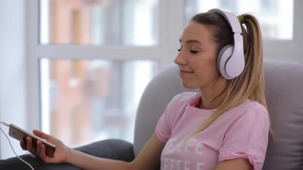 Las mujeres se relajan en casa con una taza de té y buena música en los auriculares — Vídeos de Stock