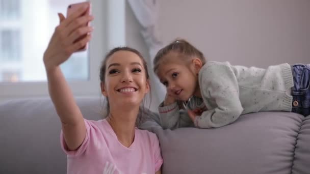 Giovane madre con sua figlia fare un selfie seduto sul divano a casa — Video Stock
