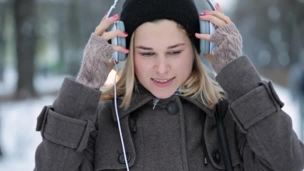 Женщина слушает музыку, одевает наушники в зимнем городе — стоковое видео