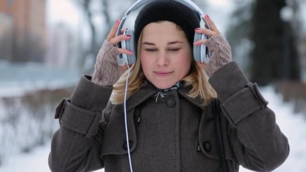 Mujer escuchando música viste los auriculares en la ciudad de invierno — Vídeos de Stock