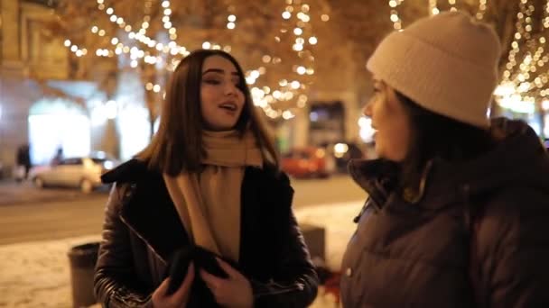Щасливі дівчата гуляють по нічній алеї, прикрашеній гірляндою і розмовляють — стокове відео