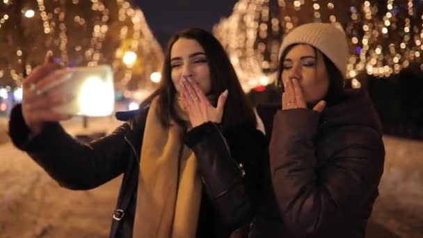 Meninas amigas fazendo selfie vídeo enviar beijo arejado no chat à noite beco decorado por guirlanda — Vídeo de Stock