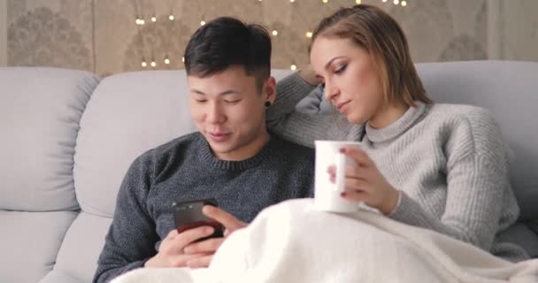 Mladý pár pomocí chytrého telefonu sedí na gauči doma