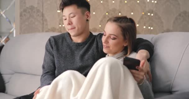Giovane coppia utilizzando smartphone seduto sul divano a casa — Video Stock