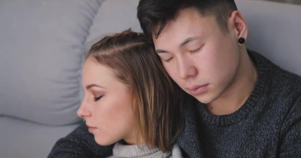 Sad young couple sit together on sofa and hug — Stock Video