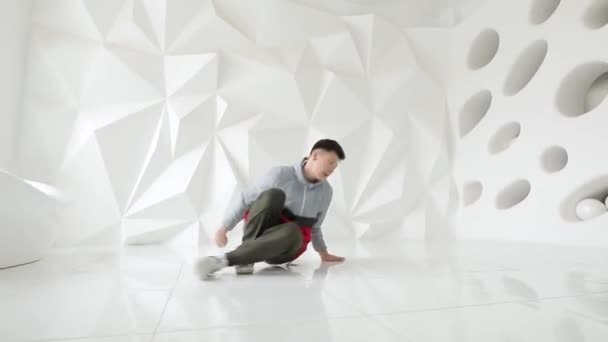Человек-брейкдансер исполняет крутые танцевальные движения на полу в белой студии — стоковое видео