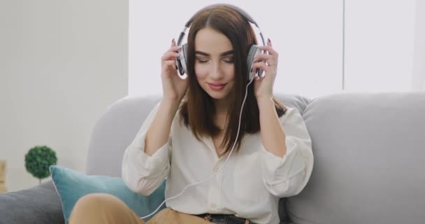 女性の大きなヘッドフォンで家で音楽を聴く — ストック動画