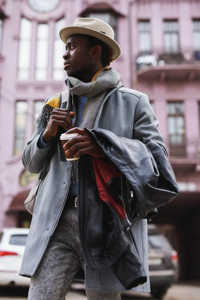 Fashion model african american man in coat and hat walking along city street