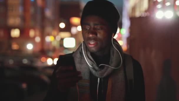 Fechar de homem africano ouvindo música em fones de ouvido à noite — Vídeo de Stock