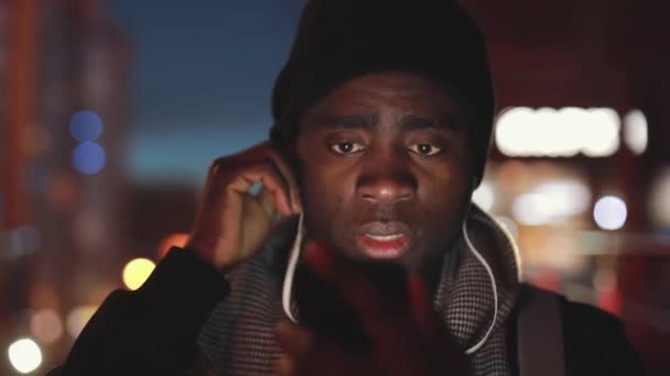 Primer plano del hombre africano escuchando música en auriculares por la noche — Vídeo de stock