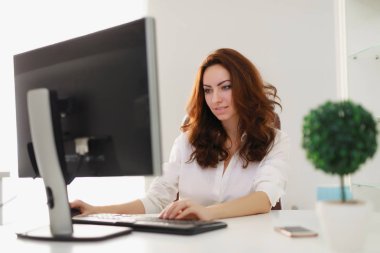 Güzel iş kadını beyaz ofiste bilgisayar monitörü seyir çalışma