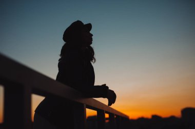 Kadın silüeti düşünüyor ve gelecekle ilgili günbatımında şehirde rüyalar.