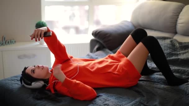 Jovem menina sexy fala por smartphone, vídeo online conversando deitado em casa cama — Vídeo de Stock