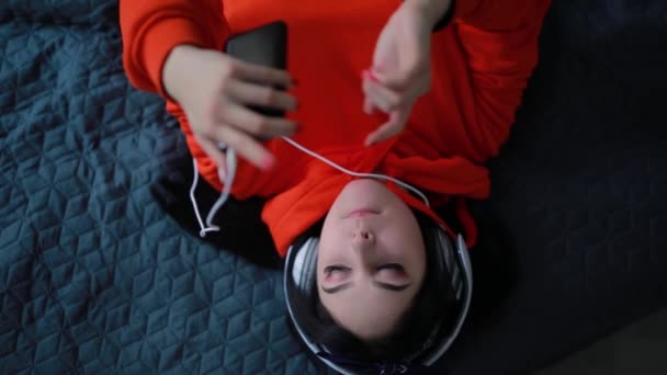 Chica escuchando música en los auriculares acostados en la cama, vista superior — Vídeos de Stock