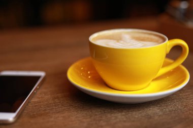 Kahve molası, latte sarı Kupası ve smartphone bir masa üzerine