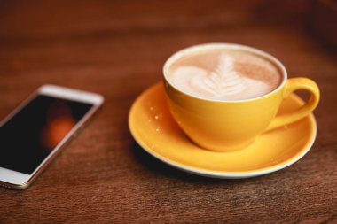 Kahve molası, latte sarı Kupası ve smartphone bir masa üzerine