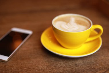 Kahve molası, latte sarı Kupası ve smartphone bir masa üzerine