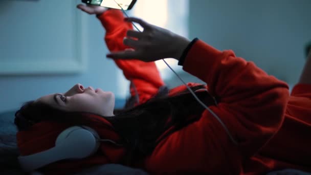 Fille écouter de la musique dans les écouteurs couché sur le lit — Video