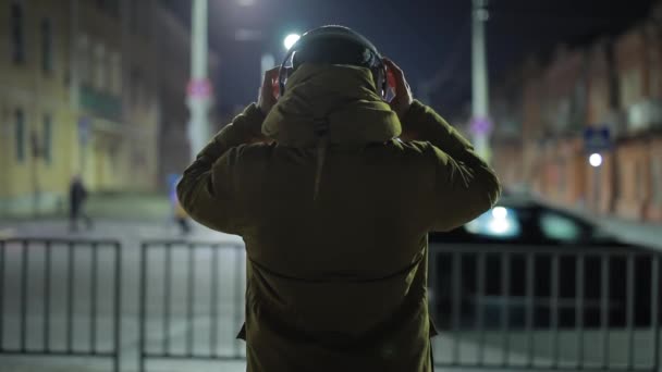 Неузнаваемый человек слушает музыку в наушниках в ночном городе — стоковое видео